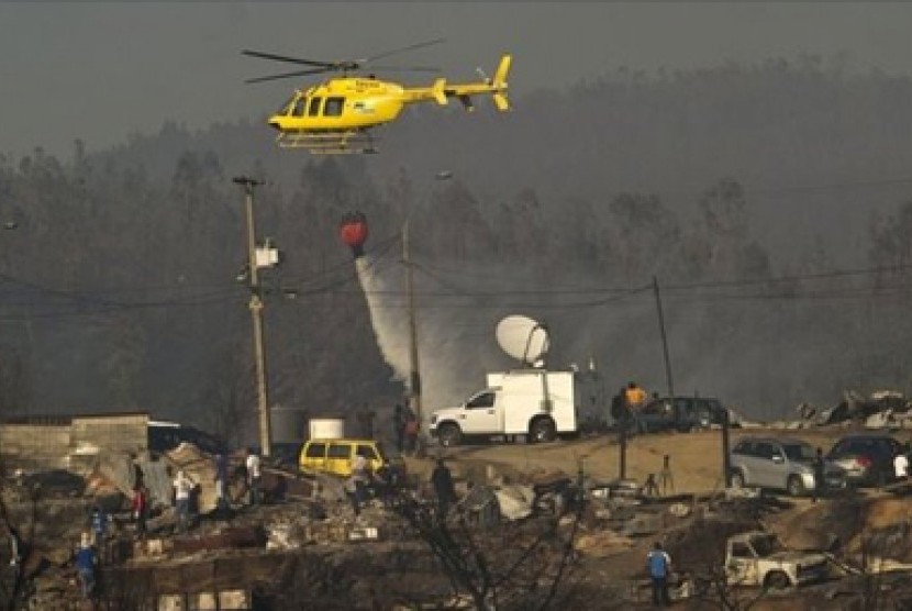 Pemadam kebakaran menggunakkan helikopter untuk menyiramkan air di puing bekas kebakaran.