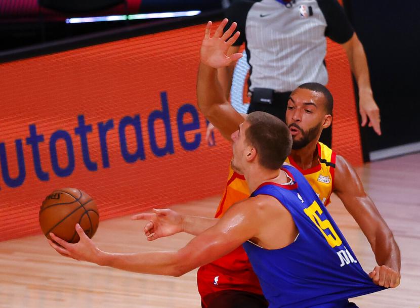 Pemain Denver Nuggets Nikola Jokic (kiri) memasukkan bola dijaga pemain Utah Jazz Rudy Gobert.