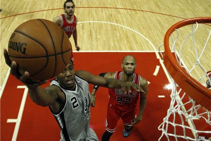 Pemain San Antonio Spurs, Kawhi Leonard (kiri), 'terbang' menjaringkan bola melawan pemain Chicago Bulls, Joakim Noah (tengah) dan Taj Gibson, di kompetisi NBA di Chicago pada Senin (11/2). 