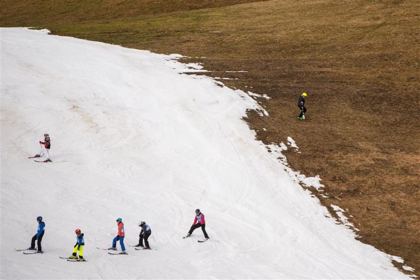 Pemain ski menuruni lereng bersalju di lereng bukit yang tidak bersalju (ilustrasi).