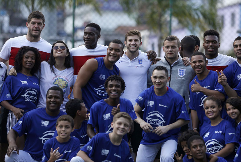 Pemain Timnas Inggris berposes bersama warga Brasil saat mereka mengunjungi kompleks olahraga di Ricinha di Rio de Janeiro pada Senin (9/6). 