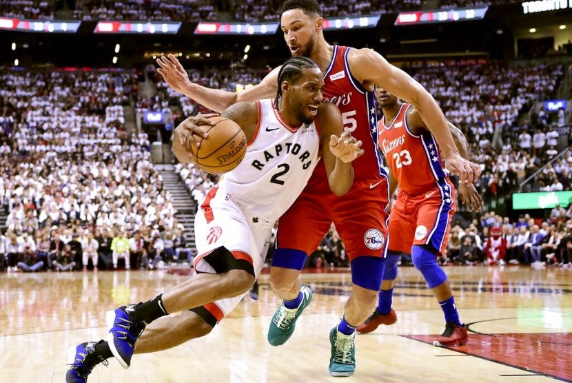 Pemain Toronto Raptors Kawhi Leonard membawa bola melewati pemain Philadelphia 76ers Ben Simmons.