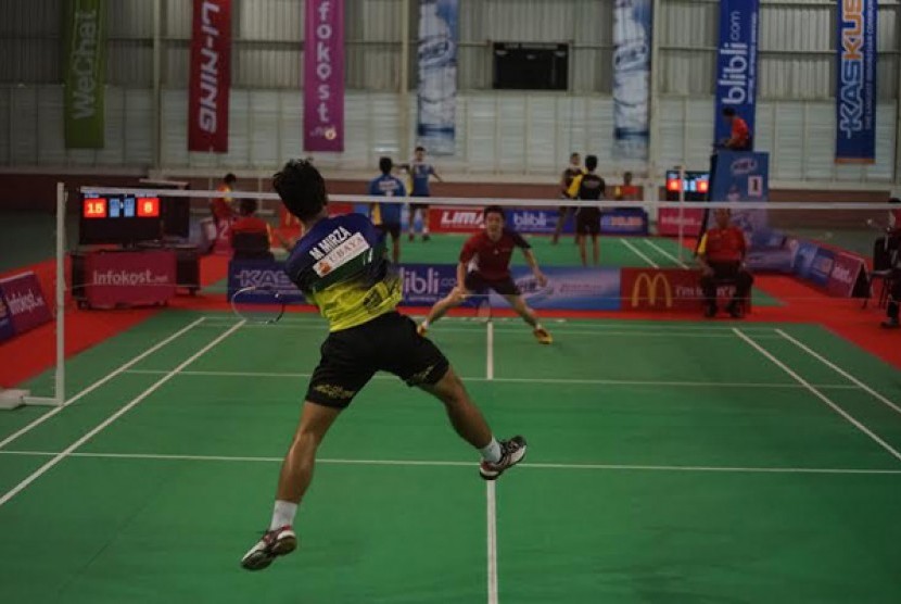 Pemain Universitas Surabaya (UBAYA) M Mirza (baju biru) melakukan smash ke daerah pertahanan pemain UPH Vicky Vendi dalam LIMA Badminton Putra
