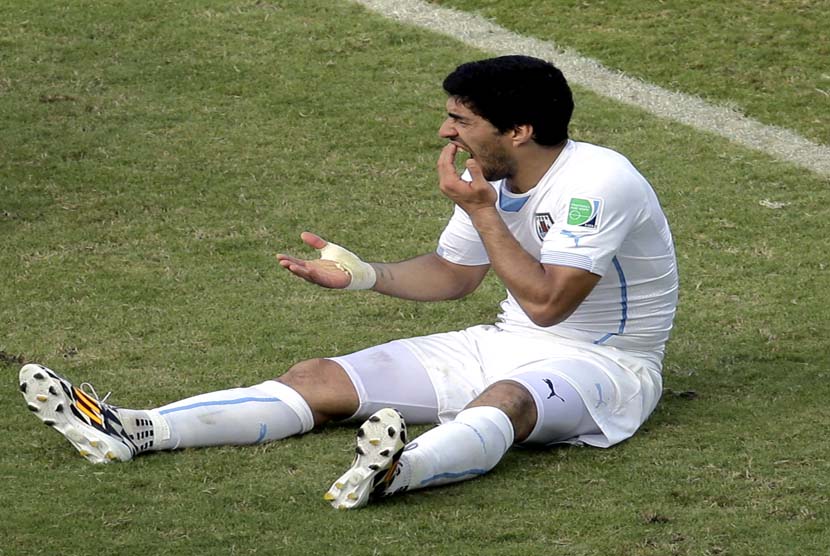 Pemain Uruguay Luis Suarez memegang giginya setelah menjalankan ke bahu Italia Giorgio Chiellini selama grup D Piala Dunia pertandingan sepak bola antara Italia dan Uruguay di Arena das Dunas di Natal, Brasil, Selasa, Selasa (24/6). (Pemain Uruguay Luis Su