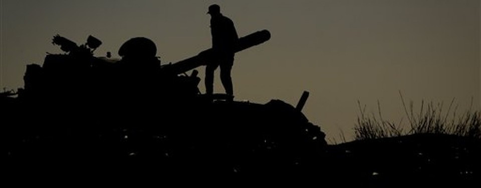 Pemberontak berdiri di atas tank tentara Moamar Qadafi yang hancur diserang pesawat NATO.