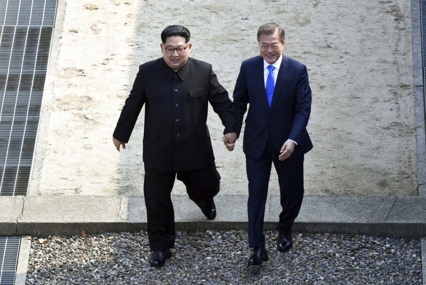Pemimpin Korea Utara Kim Jong-un (kiri) dan Presiden Korea Selatan bergandeng tangan melangkah melewati perbatasan negara di Desa Panmunjom di Zona Demiliterisasi, Jumat (27/4).