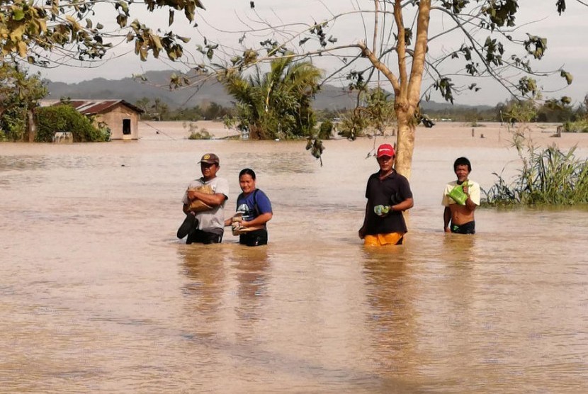 Penduduk desa di Filipina berjalan saat banjir akibat Topan Phanfone. Sedikitnya 28 orang dipastikan meninggal dunia akibat Topan Phanfone di Filipina.