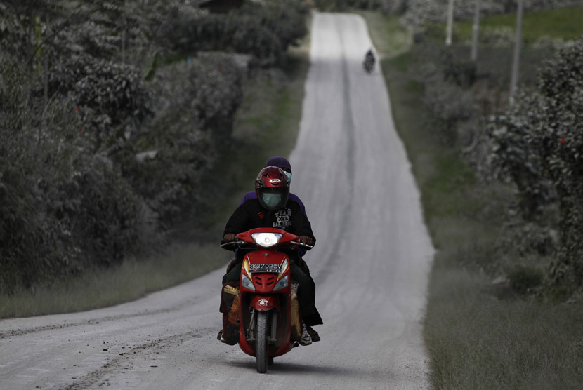  Penduduk desa naik sepeda motor melintasi jalan raya yang tertutup abu Gunung Sinabung di Desa Sigarang Garang di Kabupaten Karo, Sumut, Senin (25/11).     (Reuters/Beawiharta)