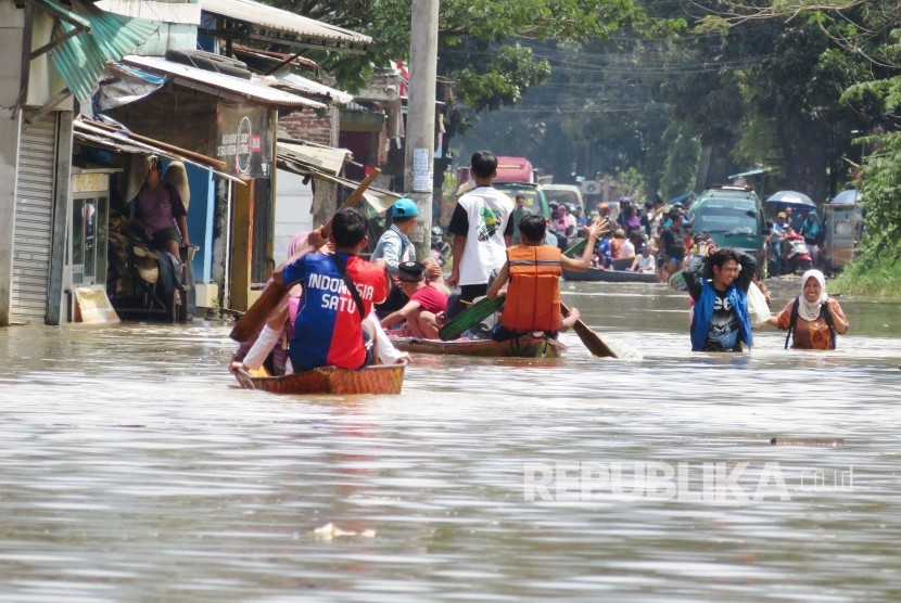 Penduduk menggunakan perahu menyusuri jalan yang telah terendam banjir luapan Sungai Citarum, di Kecamatan Baleendah, Kabupaten Bandung, Ahad (25/2).