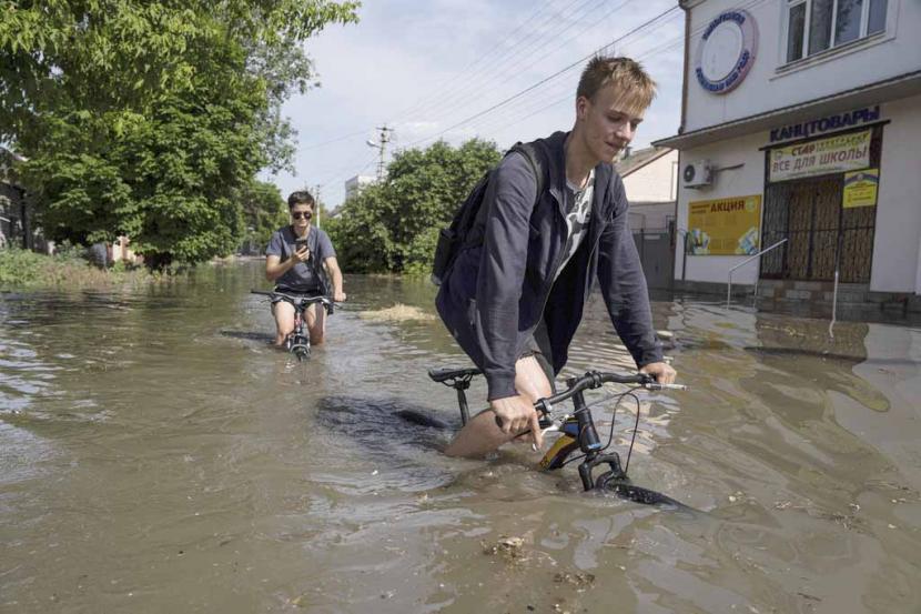 Penduduk setempat mencoba mengendarai sepeda mereka di sepanjang jalan yang banjir setelah bendungan Kakhovka meledak semalaman, di Kherson, Ukraina, Selasa, 6 Juni 2023.