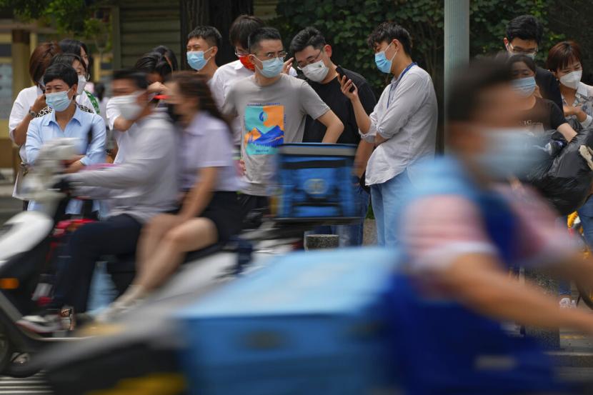 Pengendara melewati pejalan kaki yang mengenakan masker menunggu untuk menyeberang di persimpangan di Beijing, Rabu, 6 Juli 2022.