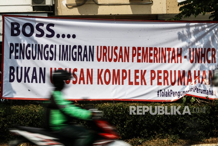 Pengendara melintas di depan spanduk penolakan keberadaan para pencari suaka di Kalideres, Jakarta, Selasa (16/7/2019). 