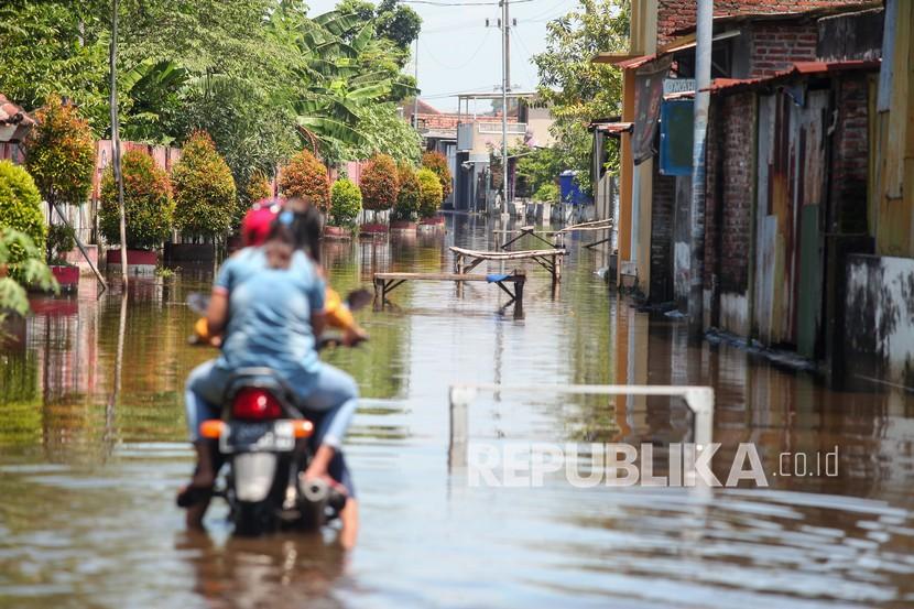 Pengendara melintas di jalan yang tergenang air di kawasan Gempolsari, Tanggulangin, Sidoarjo, Jawa Timur. Pemkab Sidoarjo melakukan normalisasi sungai untuk pengairan lahan pertanian.
