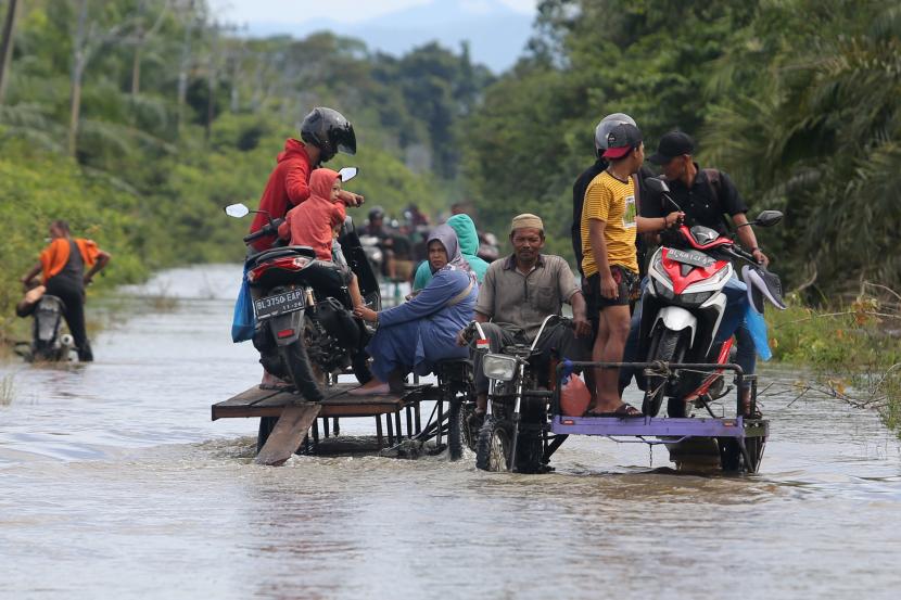Pengendara memanfaatkan jasa angkut kendaraan roda dua untuk melintasi jalan yang terendam banjir di Desa Layung, Bubon, Kabupaten Aceh Barat, Provinsi Aceh, Jumat (2/9/2022). 