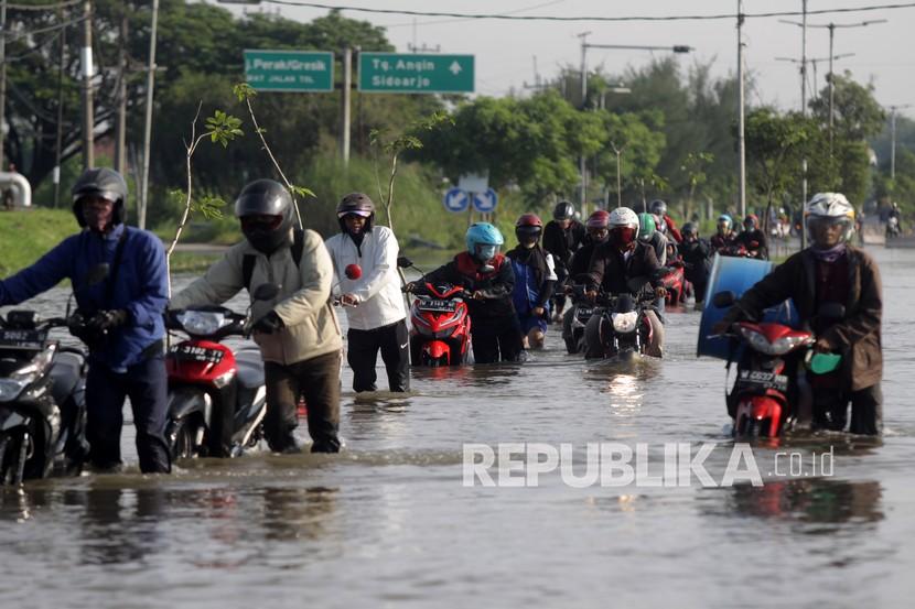 Pengendara mendorong sepeda motor menerobos banjir yang menggenangi jalan raya Porong, Sidoarjo, Jawa Timur, Selasa (16/2/2021). Curah hujan yang tinggi sejak Senin (15/2) malam mengakibatkan banjir yang merendam jalan raya Porong sehingga mengganggu kelancaran transportasi umum.
