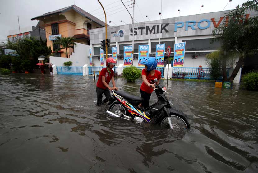 Pengendara menuntun sepeda motornya melintasi banjir di Jl. Patimura, Semarang, Jawa Tengah