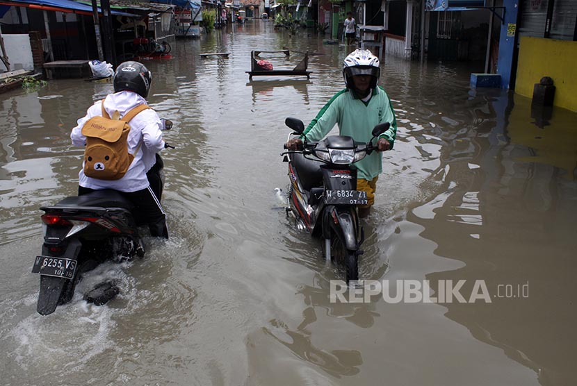 Pengendara menuntun sepeda motornya melintasi daerah banjir 