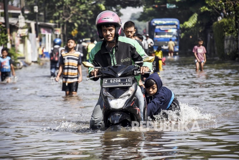 Pengendara motor dibantu sejumlah anak menerobos genangan banjir luapan Sungai Citarum, di ruas Jalan Raya Dayeuhkolot, Kabupaten Bandung, Rabu (18/12).