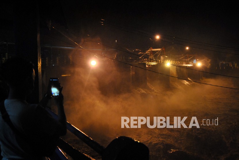 Pengendara motor melintas di atas jembatan sungai Warga memotret derasnya debit air sungai Ciliwung di Bendung Katulampa, Kota Bogor, Jawa Barat, Senin (21/9/2020). Tingginya intensitas curah hujan di wilayah Puncak, Kabupaten Bogor menyebabkan ketinggian muka air di Bendung Katulampa mengalami peningkatan hingga mencapai 250 cm atau status Siaga 1 sehingga warga di bantaran Sungai Ciliwung diminta untuk waspada.