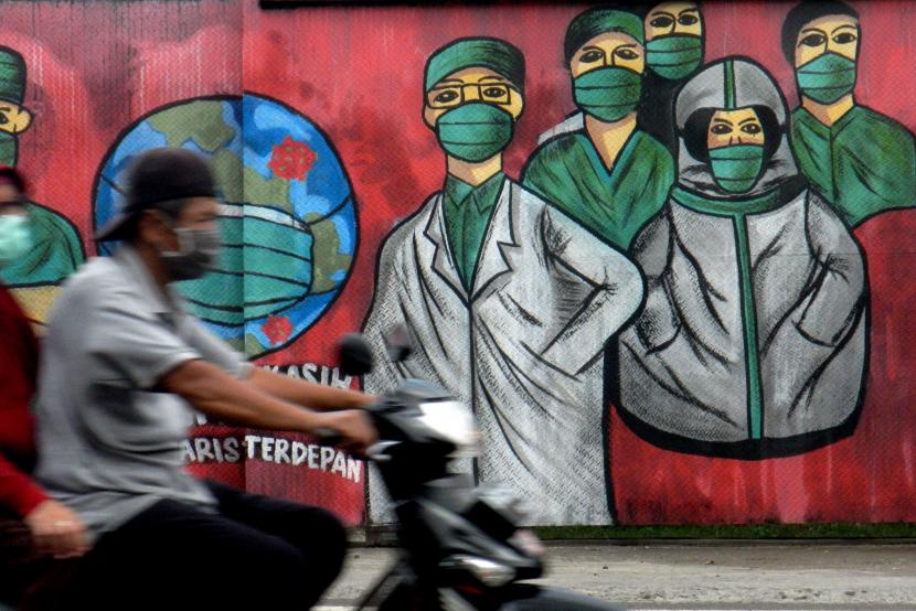 Pengendara motor melintas di depan mural tentang pandemi virus corona atau COVID-19 di Jalan Raya Jakarta-Bogor, Depok, Jawa Barat, Jumar (3/4/2020). Mural tersebut ditujukan sebagai bentuk dukungan kepada tenaga medis yang menjadi garda terdepan dalam menghadapi COVID-19 di Indonesia.