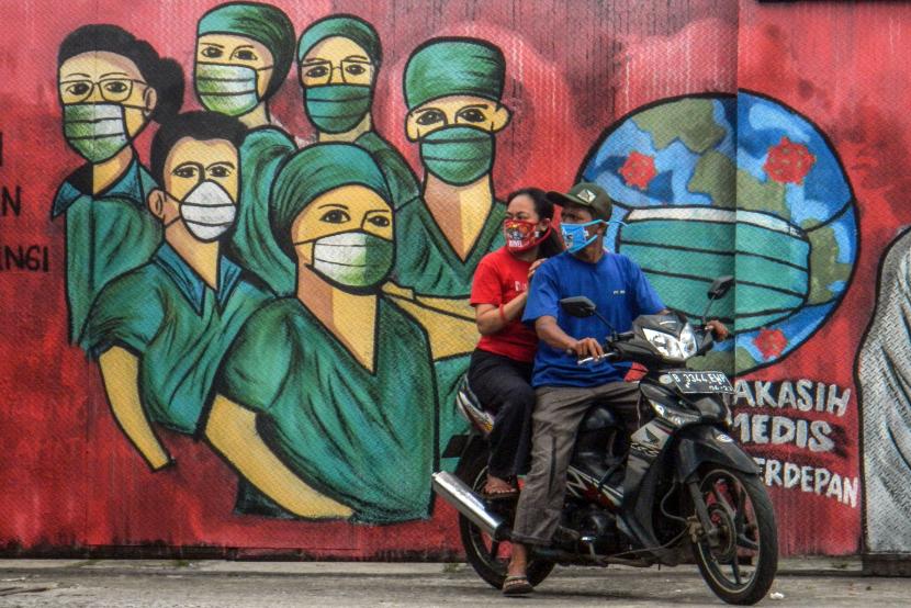 Pengendara motor melintas di depan mural tentang pandemi virus corona atau Covid-19. Per Senin (1/6), DKI Jakarta mencatat tambahan satu kasus meninggal Covid-19.