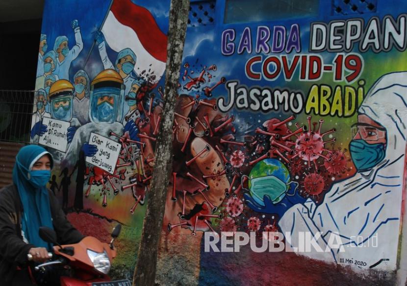 Pengendara motor melintas di depan mural yang bergambar mural seputar pandemi corona. Ada banyak lini industri yang terdampak secara ekonomi akibat Covid-19, salah satunya adalah perusahaan pers dan media massa.