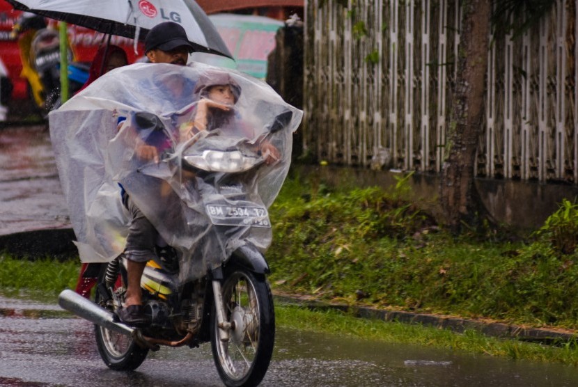 Pengendara motor menggunakan mantel saat melintas di tengah hujan turun di Kota Pekanbaru, Riau, Kamis (14/2/2019).