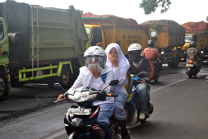 Pengendara motor menutup hidungnya saat melintasi sejumlah truk sampah milik Dinas Kebersihan dan Pertamanan Kota Bogor yang diparkir di pinggir jalan raya Paledang, Kota Bogor, Jawa Barat, Senin (4/1).