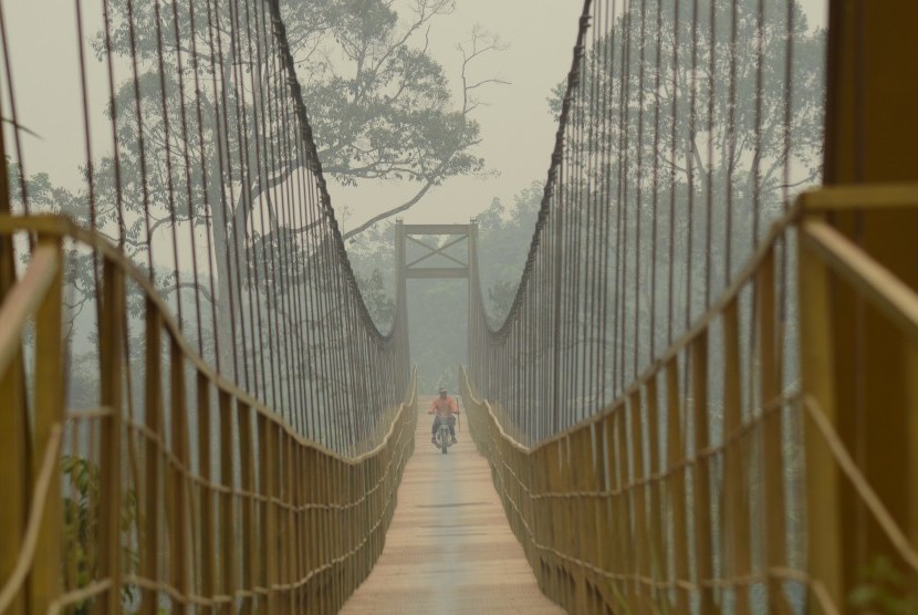 Pengendara roda dua menyeberangi jembatan yang diselimuti kabut asap di Desa Aur Gading, Batin XXIV, Batanghari, Jambi, Minggu (25/10). 