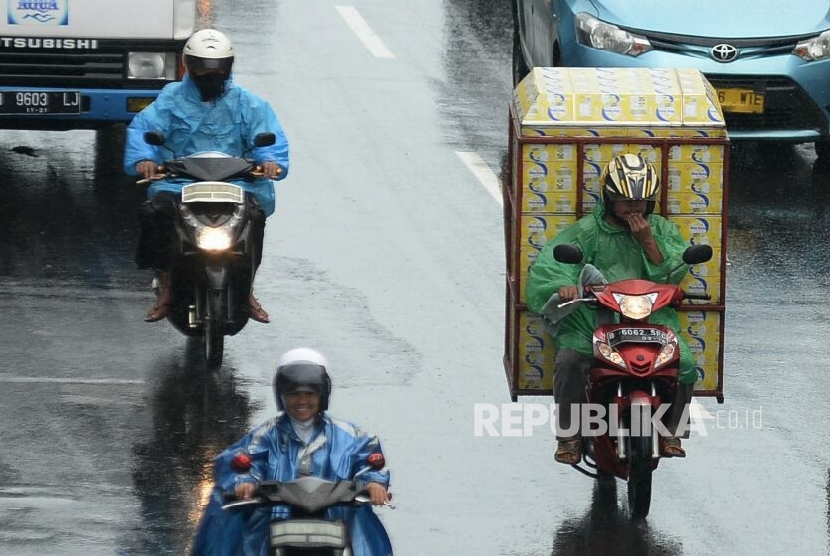  Pengendara sepeda motor dengan menggunakan jas hujan menerobos hujan di Kawasan Salemba, Jakarta, Senin (5/12).