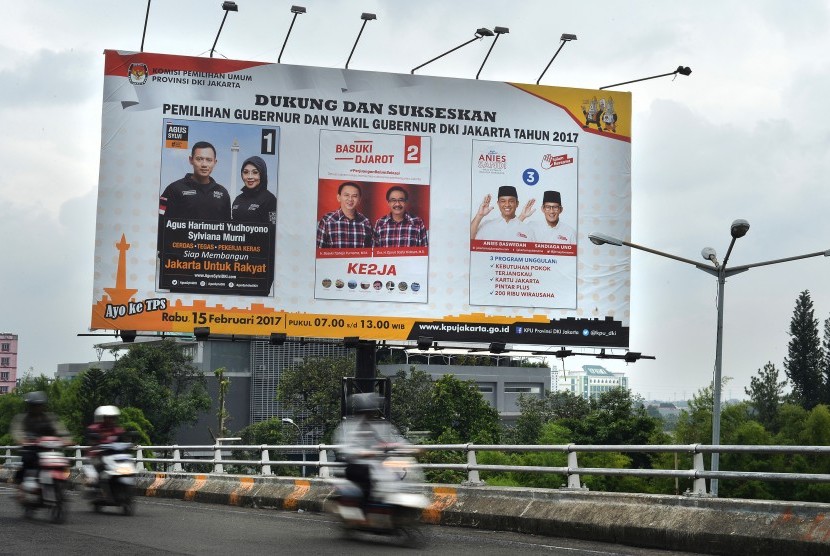 Pengendara sepeda motor melintas di dekat baliho sosialisasi Pilkada Gubernur dan Wakil Gubernur DKI Jakarta Tahun 2017 di Jakarta, Jumat (10/2).