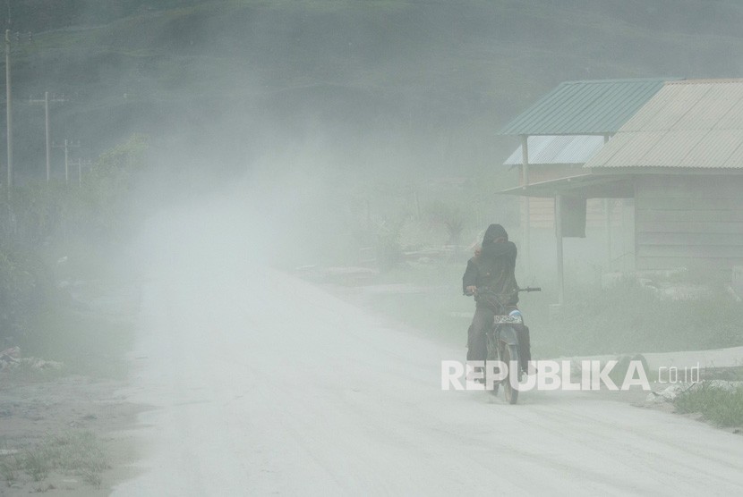 Pengendara sepeda motor melintas di jalan yang dipenuhi debu vulkanik erupsi Gunung Sinabung, di Desa Naman Teran, Karo, Sumatera Utara, Kamis (28/12). 