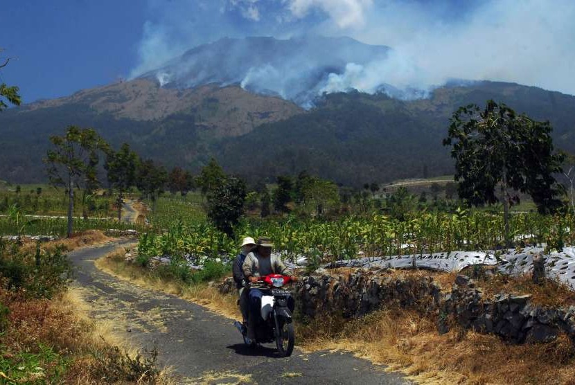 Pengendara sepeda motor melintas di perladangan berlatar belakang kebakaran hutan gunung Sumbing Desa Pagergunung, Bulu, Temanggung, Jawa Tengah, Selasa (11/9). 