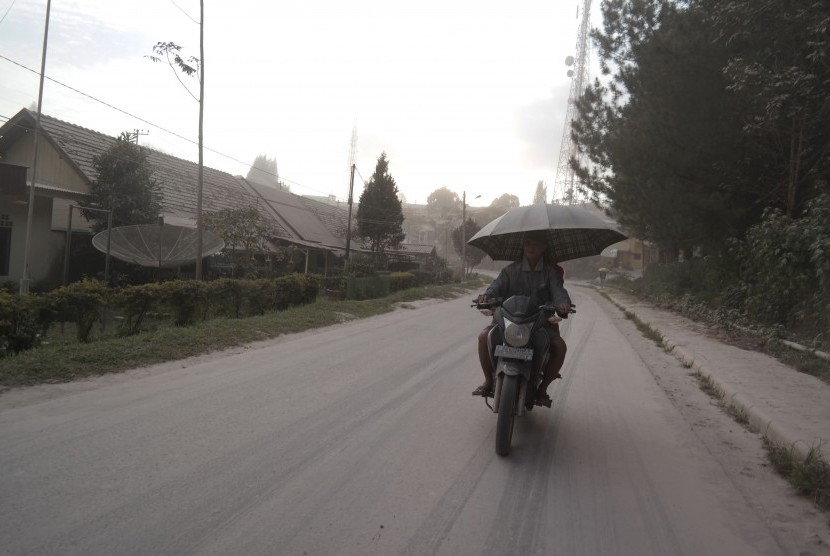 Pengendara sepeda motor melintas saat hujan abu vulkanik erupsi Gunung Sinabung, di Brastagi, Karo, Sumatera Utara, Jumat (26/6).