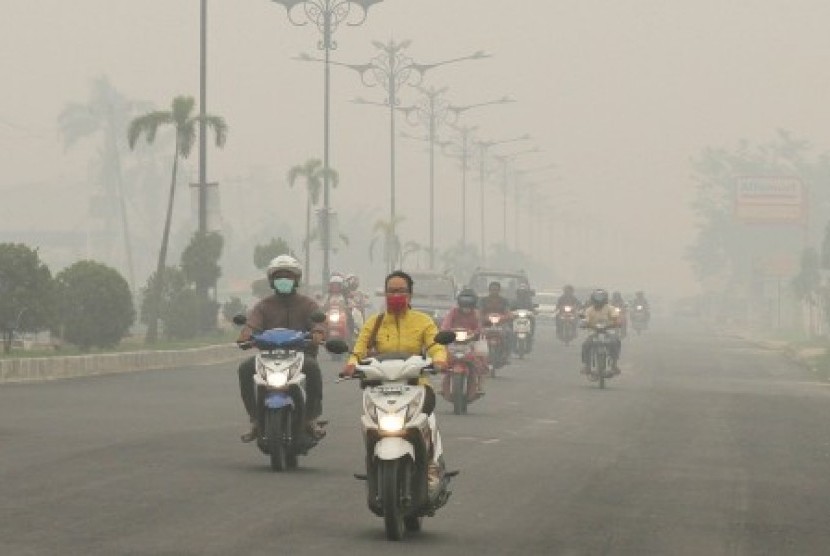 Pengendara sepeda motor melintasi jalan ketika kabut asap pekat menyelimuti Kota Pekanbaru, Riau, Minggu (4/10).