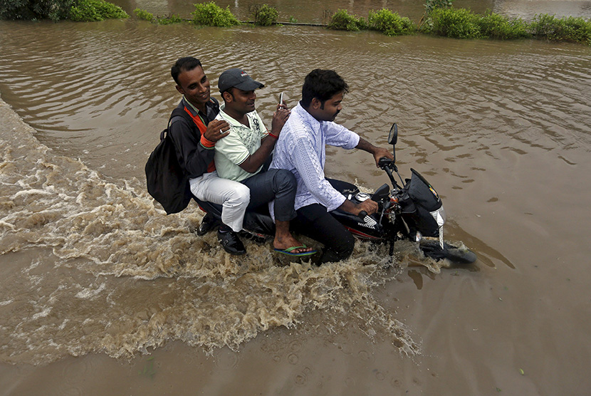  Pengendara sepeda motor melintasi jalan yang terendam air banjir, usai hujan deras di Ahmedabad, India, Selasa (28/7).