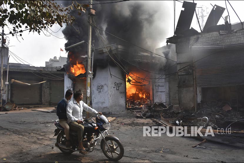 Kisah Seorang Muslim Selamat Saat Kerusuhan New Delhi. Pengendara sepeda motor melintasi sebuah toko yang dibakar oleh massa di New Delhi, India, Rabu (26/2). (Dinesh Joshi/AP)