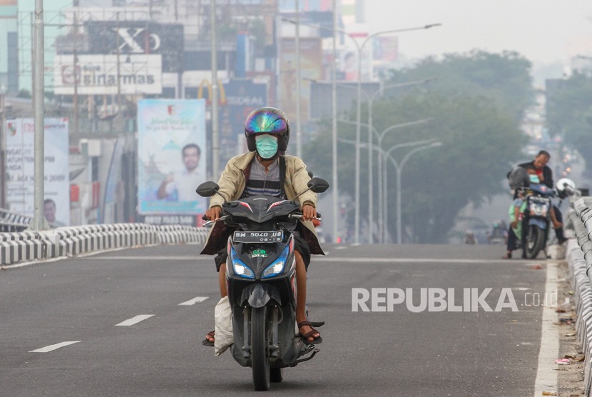 Pengendara sepeda motor menggunakan masker pelindung pernapasan ketika kabut asap karhutla menyelimuti Kota Pekanbaru, Riau, Selasa (30/07/2019). 