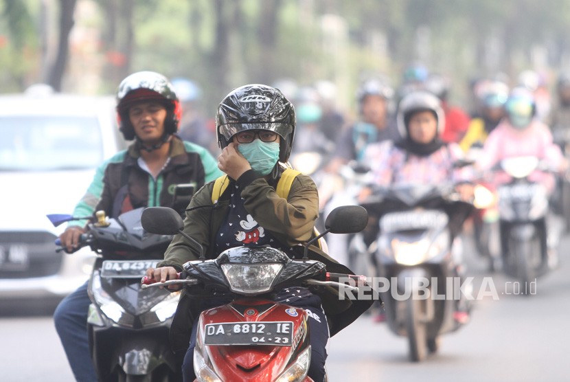Pengendara sepeda motor menggunakan masker pelindung pernapasan saat melintas di jalan Brig Jend Hasan Basri yang diselimuti kabut asap di Banjarmasin, Kalimantan Selatan, Senin (14/10/2019).