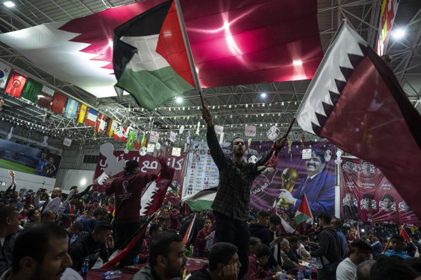 Penggemar sepak bola Palestina mengibarkan bendera Qatar dan Palestina saat mereka menonton siaran langsung pertandingan pembukaan Piala Dunia 2022 antara Qatar dan Ekuador, di gimnasium tertutup di Kota Gaza, Minggu, 20 November 2022. Piala Dunia 2022 berlangsung di Qatar.