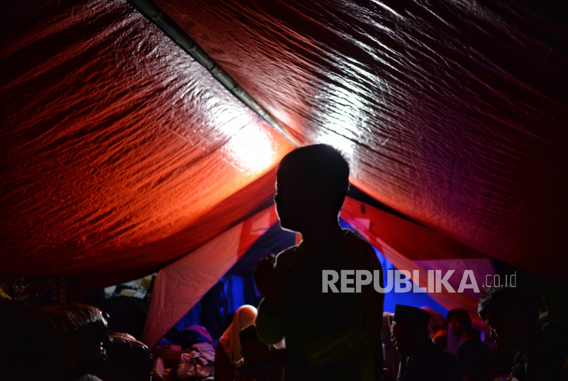 Pengungsi beraktivitas di dalam tenda darurat di Kampung Gasol, Desa Gasol, Cugenang, Kabupaten Cianjur, Jawa Barat, Ahad (27/11/2022). Beberapa pengungsi korban gempa Cianjur mengisi waktu malam hari di tenda pengungsian dengan menggelar tahlil atau menyaksikan pertandingan piala dunia. 