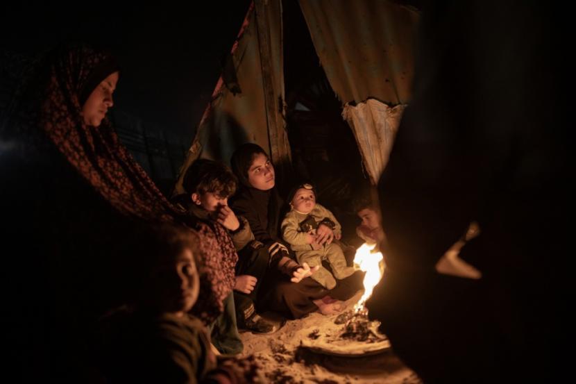 Pengungsi dari Jalur Gaza utara menghangatkan diri di dekat api unggun di luar tenda mereka di dekat perbatasan yang memisahkan Jalur Gaza dan Mesir, di kota Rafah, di Jalur Gaza Selatan.