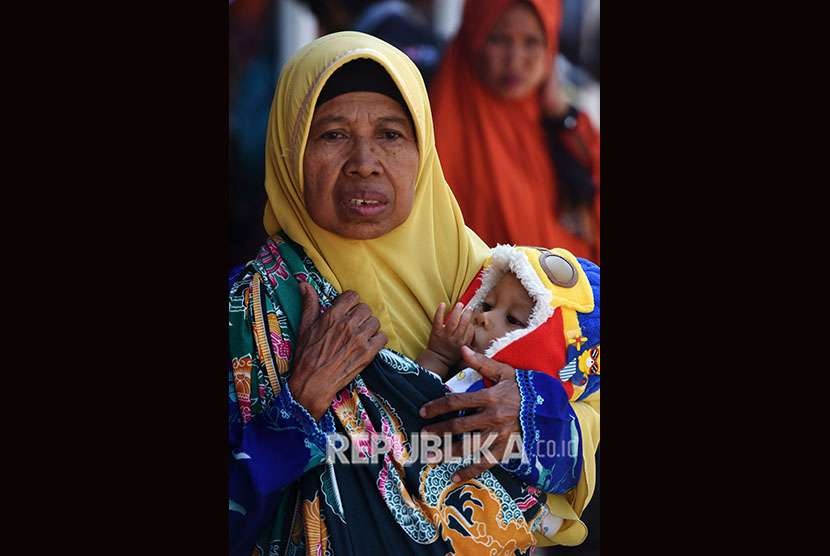 Pengungsi gempa dan tsunami Palu-Donggala menggendong cucunya saat tiba di Makassar dengan menggunakan pesawat Hercules di Lanud Hasanuddin Makassar, Sulawesi Selatan, Selasa (2/10). 