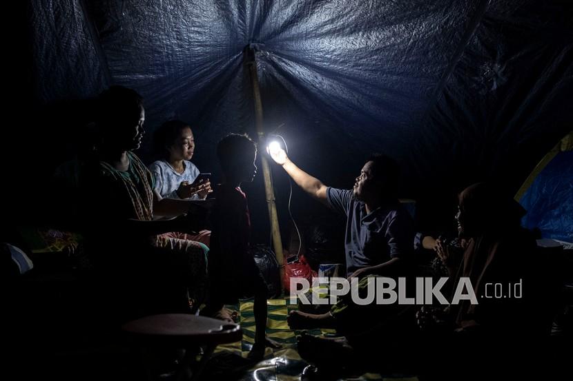 Pengungsi korban gempa bumi menyalakan lampu untuk menerangi tenda darurat yang dihuni keluarganya di kompleks Stadion Manakarra, Mamuju, Sulawesi Barat, Ahad (17/1/2021). BNPB menyatakan berdasarkan data per 17 Januari pukul 14.00 WIB jumlah korban gempa bumi Sulawesi Barat yang meninggal berjumlah 73 orang dan sebanyak 27.850 orang mengungsi di 25 titik pengungsian. 
