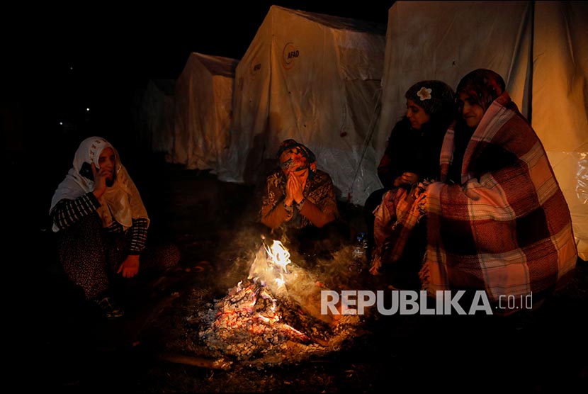 Pengungsi menghangatkan diri di dekat api di area tenda pengungsian di Elazig, Turki, Ahad (26/1). 