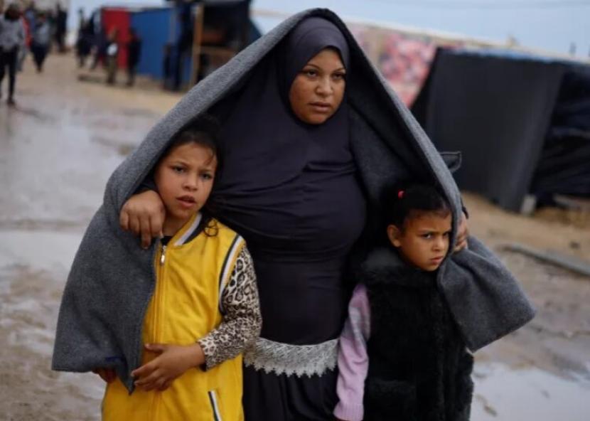 Pengungsi Palestina berjalan di sebuah kamp di Rafah, Jalur Gaza selatan, setelah hujan lebat mengguyur wilayah tersebut pada Rabu (13/12/2023).