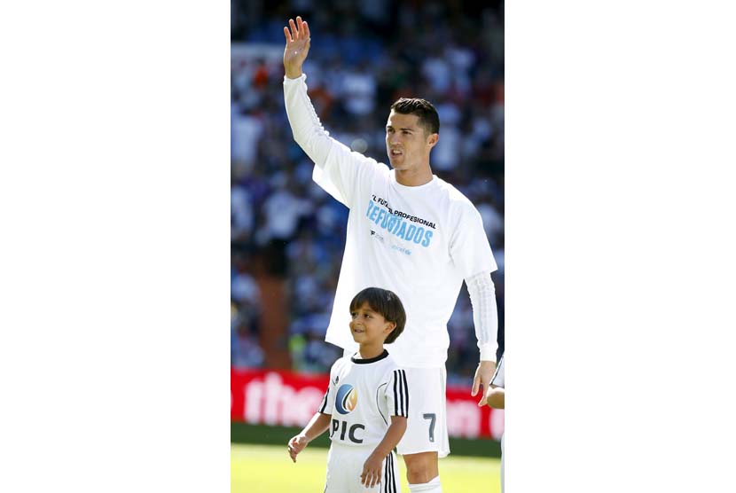 Pengungsi Suriah, Zaid (tujuh tahun), tersenyum saat menemani bintang Real Madrid, Cristiano Ronaldo, sebelum pertandingan La Liga Spanyol dengan Granada di Stadion Santiago Bernabeu, Madrid, Spanyol, Sabtu (19/9). 
