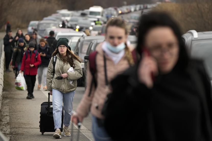 Pengungsi Ukraina berjalan di sepanjang kendaraan yang berbaris untuk menyeberangi perbatasan dari Ukraina ke Moldova, di titik perbatasan persimpangan Mayaky-Udobne dekat Udobne, Ukraina, Sabtu, 26 Februari 2022. 