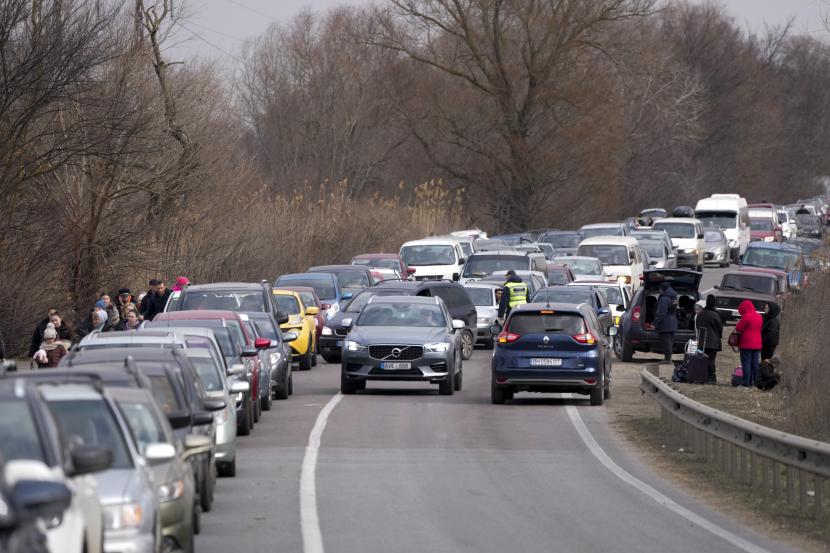 Pengungsi Ukraina berjalan di sepanjang kendaraan yang berbaris untuk menyeberangi perbatasan dari Ukraina ke Moldova, di titik perbatasan persimpangan Mayaky-Udobne dekat Udobne, Ukraina, Sabtu, 26 Februari 2022.