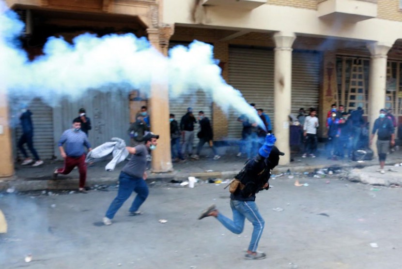Pengunjuk rasa antipemerintah berlari  melemparkan tabung gas air mata ke arah pasukan polisi anti huru hara selama bentrokan dengan pasukan polisi anti huru hara di jalan Al Rasheed  Baghdad, Irak, Senin (25/11/2019).